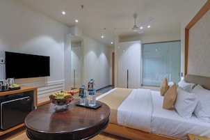 Habitación de hotel con cama, televisor, cafetera, frutero y dos botellas de agua sobre una mesa.