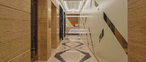 A modern hallway with marble flooring, wooden paneling, and a geometric light fixture.