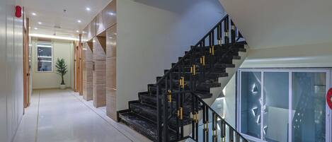 A modern staircase with black railings and marble steps, leading to a landing with a glass door.