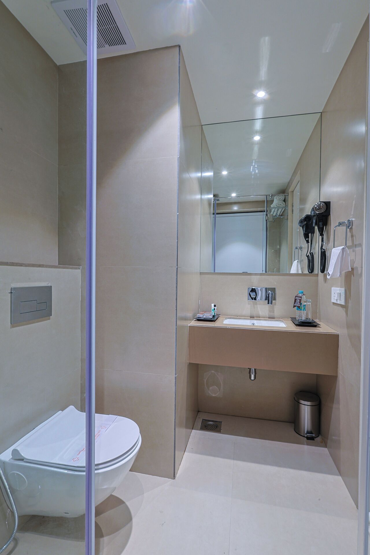 Un baño moderno con cabina de ducha de vidrio, inodoro blanco, lavabo con espejo y cubo de basura.