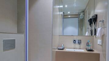 Un baño moderno con cabina de ducha de vidrio, inodoro blanco, lavabo con espejo y cubo de basura.