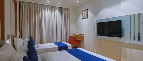 A hotel room with two beds, a desk, a chair, a ceiling fan, and a TV.