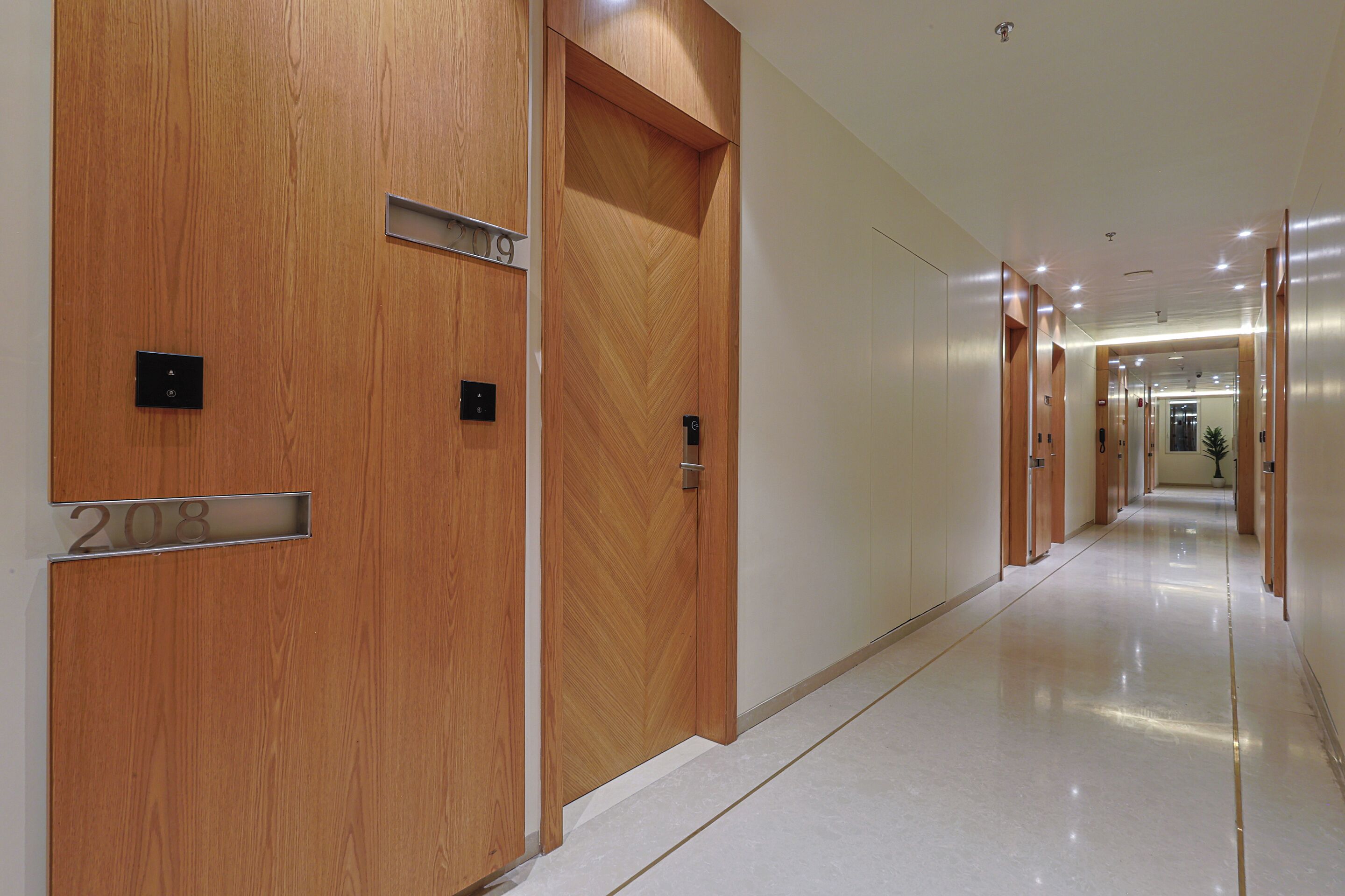 A modern hotel corridor with wooden doors marked with room numbers, a shiny tiled floor, and a long hallway with doors on both sides.