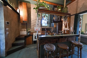 A kitchen with a wooden island, bar stools, hanging plants, and a view of the living area.