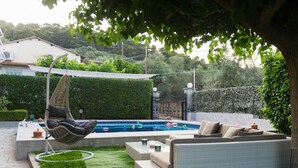 Un patio trasero con piscina, una silla colgante, un sofá y un césped bien cuidado.