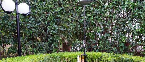 A garden area with a central white pedestal, surrounded by neatly trimmed hedges and stone pathways.