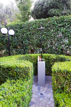 Un'area giardino curata, con un piedistallo bianco al centro, circondata da siepi ben curate e un vialetto in pietra.