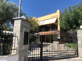 Una entrada protegida con un pilar de piedra, un portón metálico y un edificio de fachada amarilla con un área cubierta.
