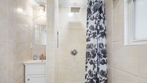A shower area with a shower curtain, a sink with a mirror, and a tiled floor.