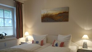 Un cuarto de hotel con una cama grande, dos mesitas de noche, una ventana con cortinas, un cuadro en la pared y una lámpara en cada mesita de noche.
