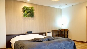 Ein Hotelzimmer mit Bett, Schreibtisch, Stuhl, Wandpflanze und Deckenleuchte.