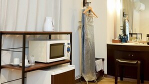 Ein Hotelzimmer mit Holzboden, einer weißen Mikrowelle, einem kleinen Tisch mit Wasserkocher, einem Kleidungsstück zum Aufhängen, einem Spiegel und einem Holzstuhl.