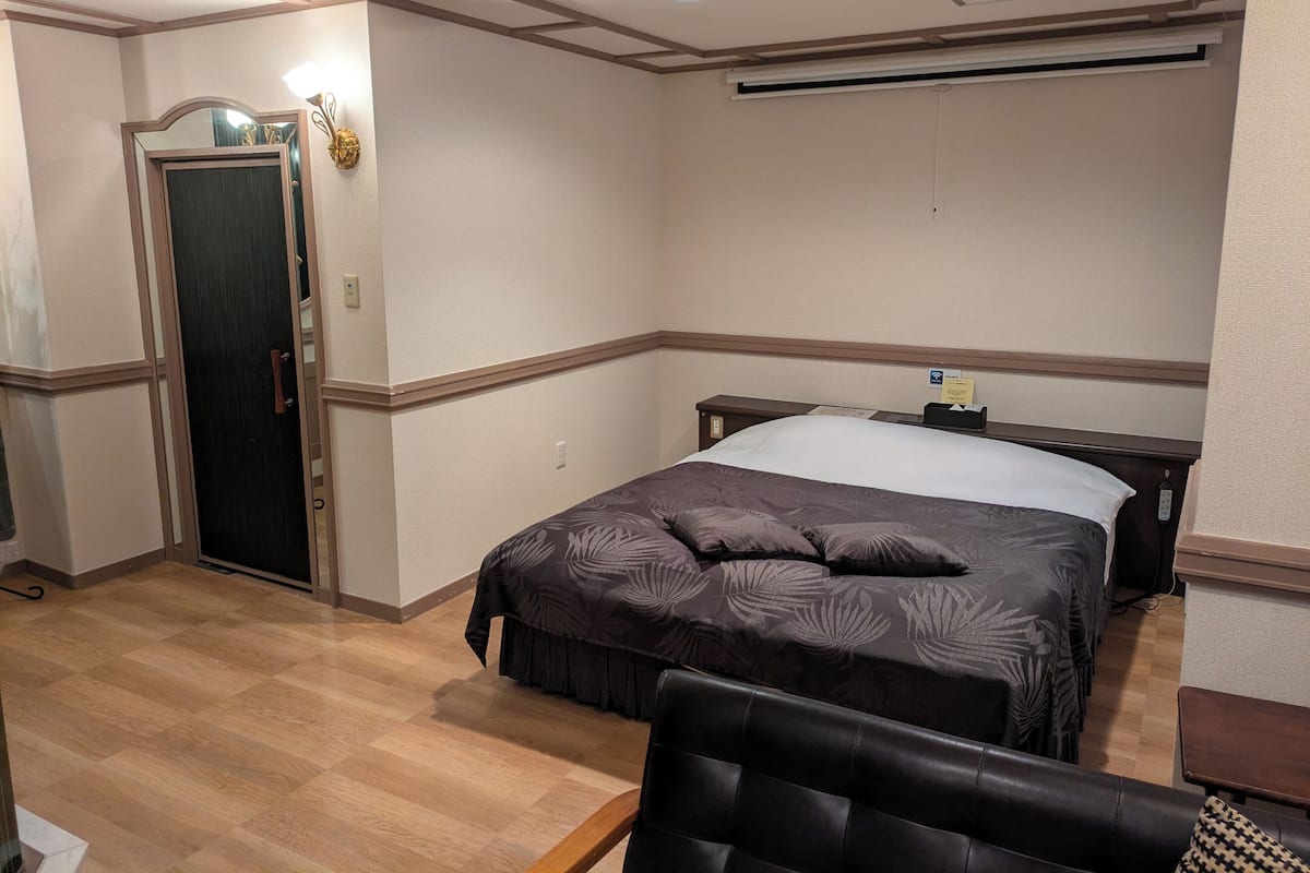 Habitación de hotel con cama, escritorio, silla, puerta e iluminación empotrada en el techo.