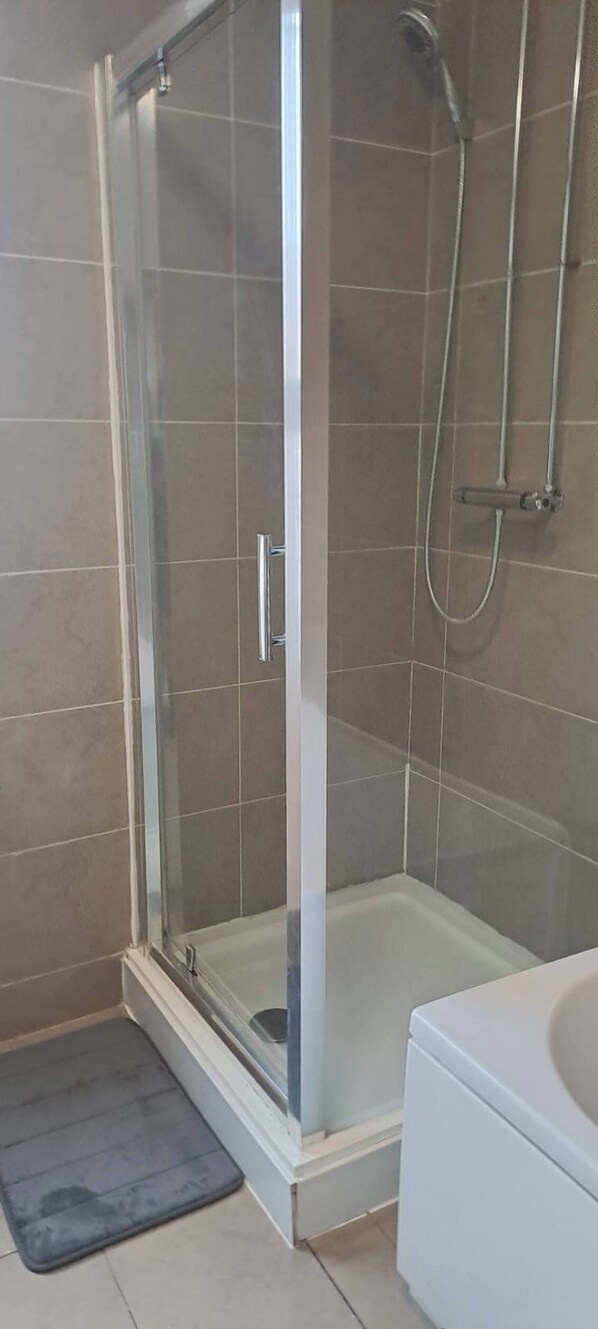 Een douche met glazen wand, een wit wastafeltje en een klein opstapje naar de douche.