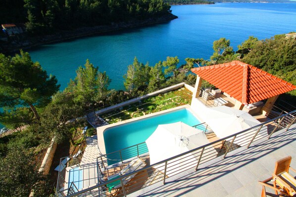 A pool area with a clear view of the sea, surrounded by trees and a building with a red roof. - Villa Lukrecia -Stunning Sea View Retreat (Korcula)