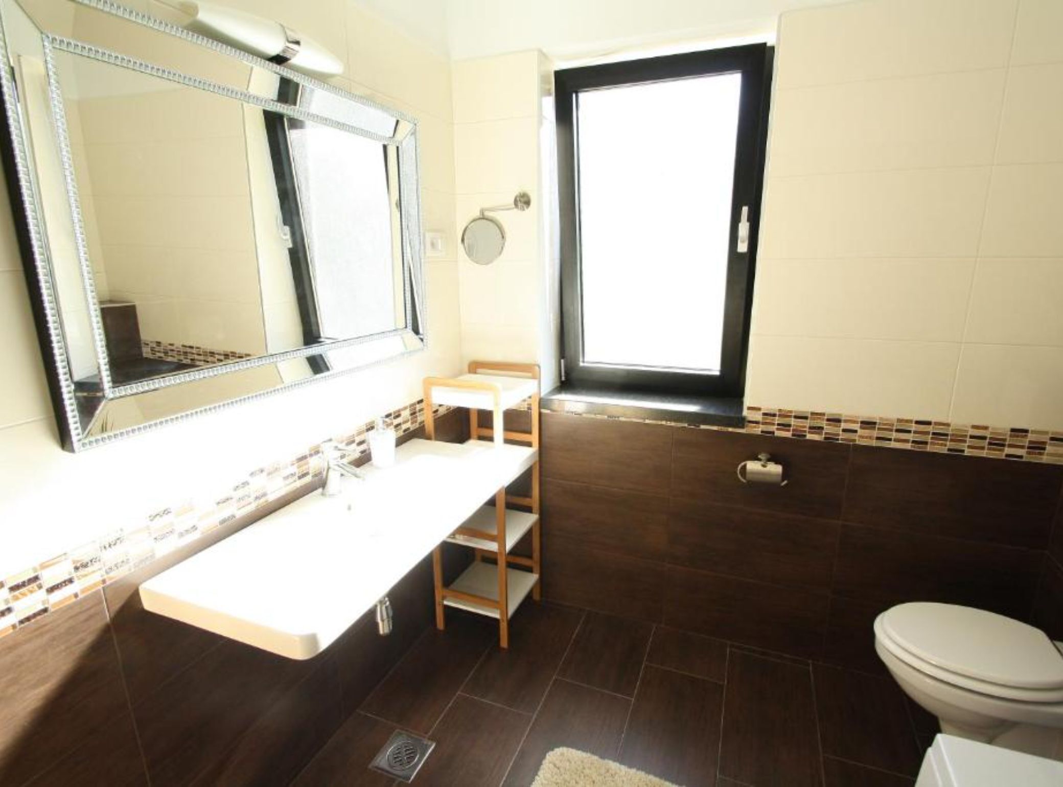 A bathroom with a large mirror, a sink, a toilet, and a window.