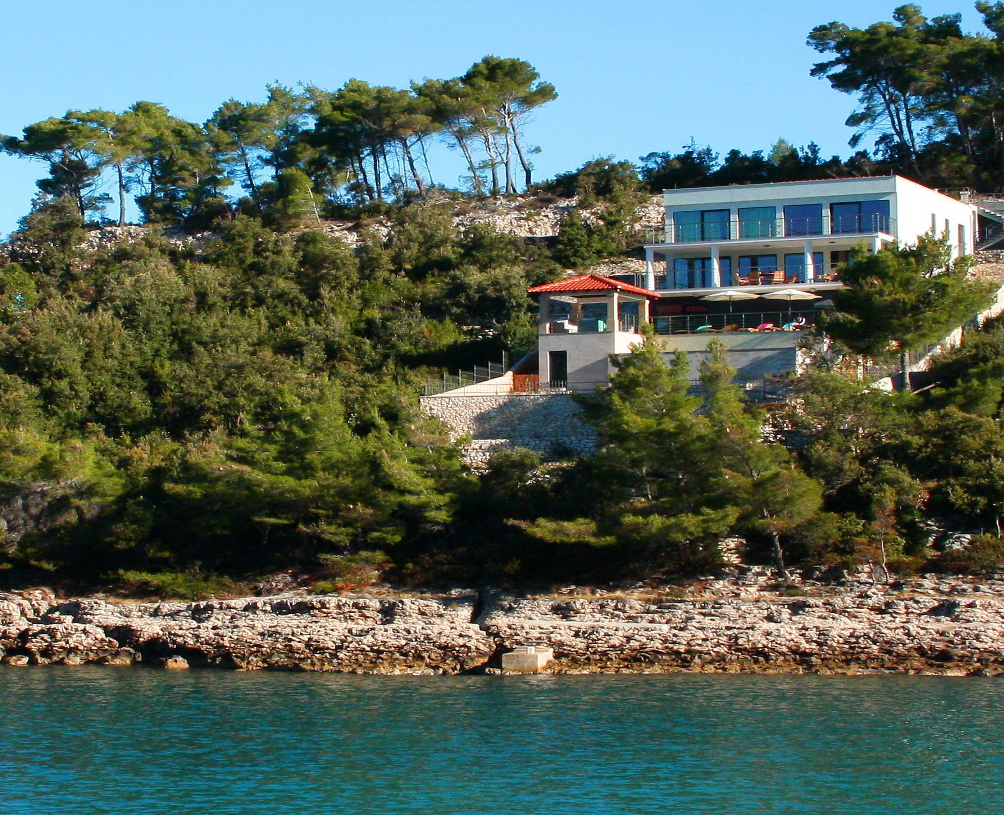 Una propiedad costera con un edificio grande, un muro de piedra y un litoral rocoso.