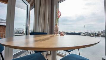 Una mesa redonda con sillas azules, un florero con flores y vistas a un puerto deportivo con barcos.