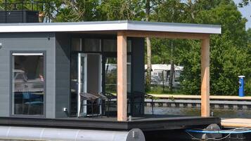 Una estructura flotante moderna con terraza cubierta, puertas de vidrio y mobiliario exterior.