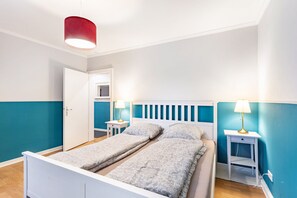 A double bed with a white headboard, two bedside tables with lamps, and a door leading to a bathroom.