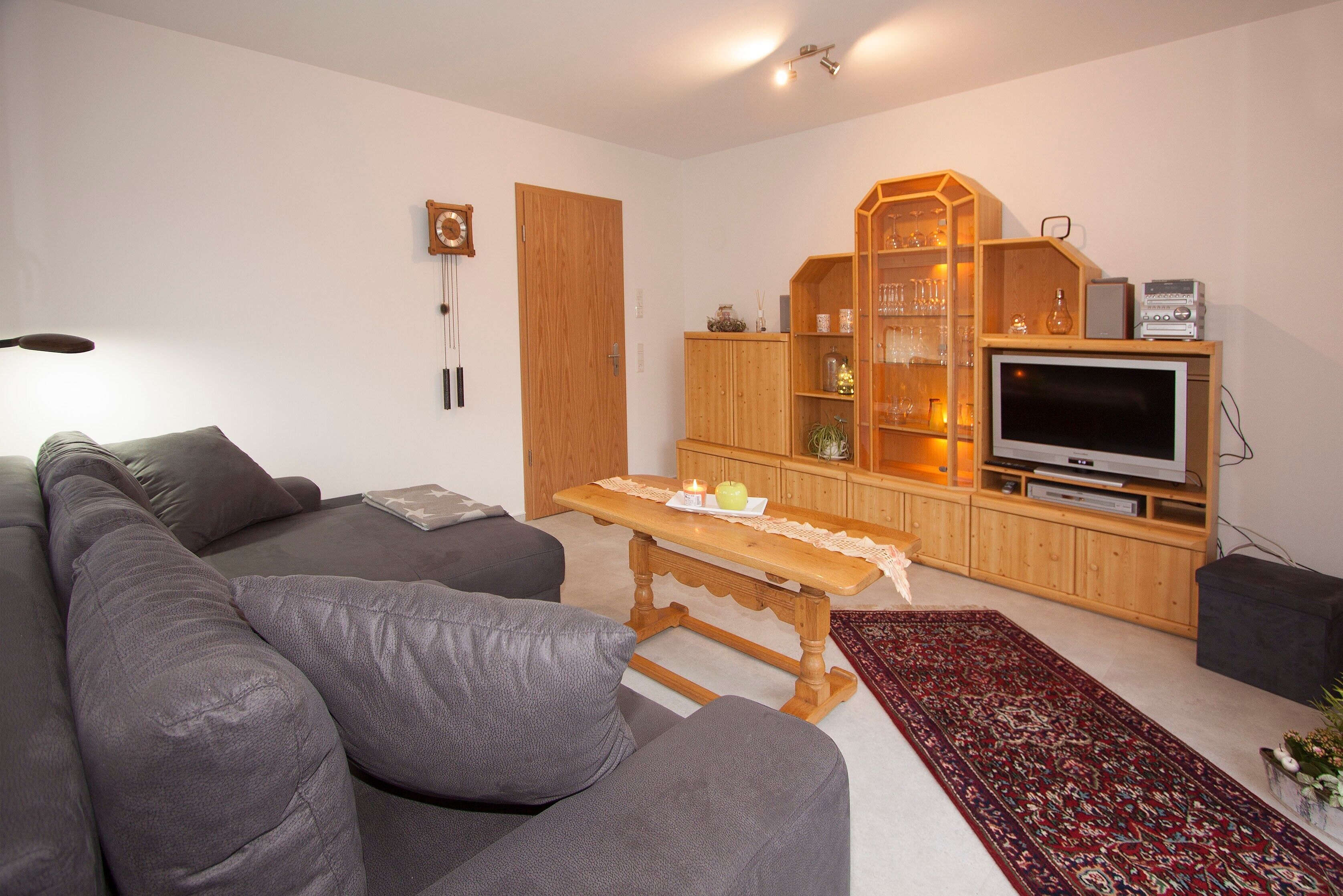 Een woonkamer met een bank, een houten kast, een televisie en een tafel met een kaars.