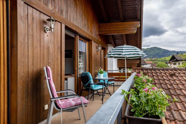 Un balcón de madera con una mesa, sillas y una planta en maceta.