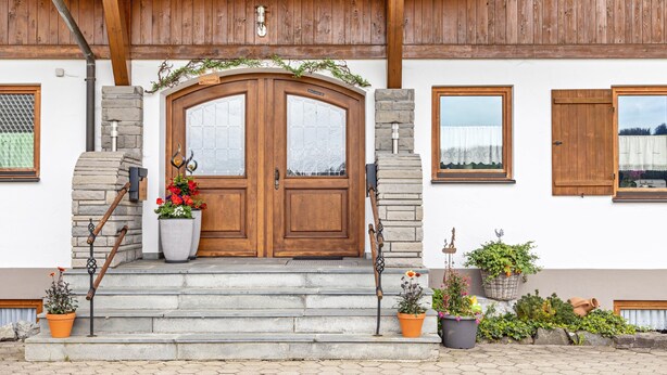 A wooden front door with a stone wall, a set of steps leading up to the entrance, and potted plants on the steps. - Apartment 'Grünten' with Mountain View, Shared Garden and Wi-Fi (Wertach)