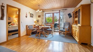 A room with a wooden ceiling, a dining table with chairs, a sofa, a cabinet, and a window with curtains. - Apartment 'Grünten' with Mountain View, Shared Garden and Wi-Fi (Wertach)