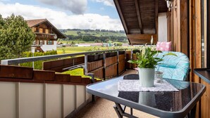 A balcony with a table, potted plant, and a view of a rural landscape. - Apartment 'Grünten' with Mountain View, Shared Garden and Wi-Fi (Wertach)