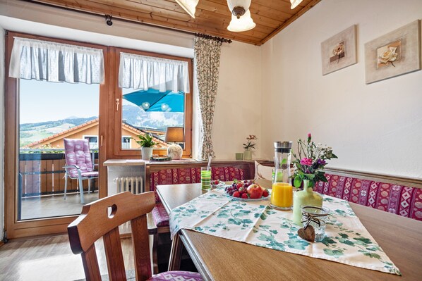 A dining area with a table set for two, a view of the outdoors, and a balcony with a chair. - Apartment 'Erd - Reuterwanne' with Mountain View, Shared Garden and Wi-Fi (Wertach)
