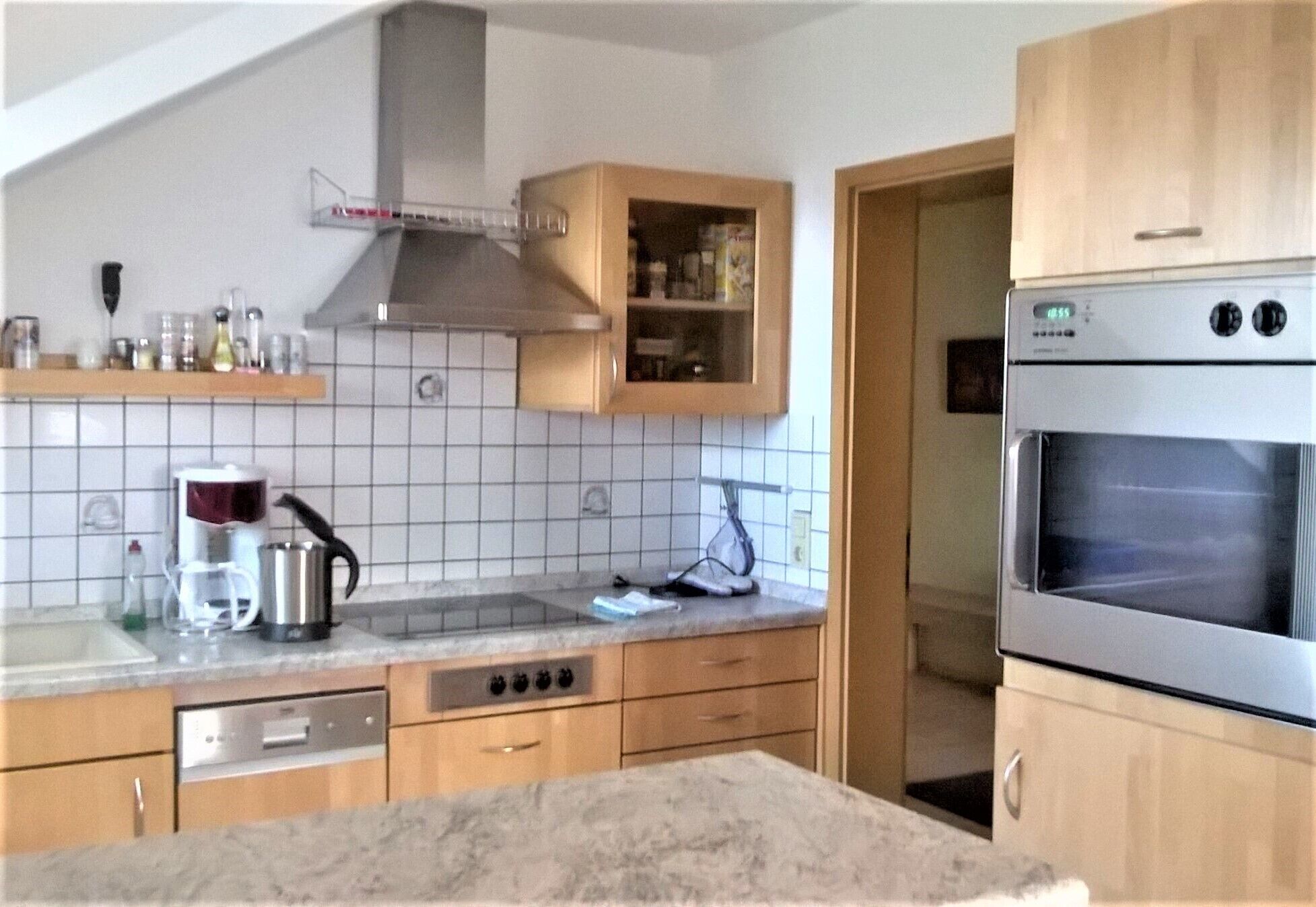 Eine Küche mit Holzausstattung, einem Edelstahlbackofen und einer gefliesten Spritzschutzwand.