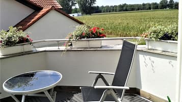 Ein Balkon mit Tisch und Stuhl, Blumentöpfen und Blick auf ein Feld.