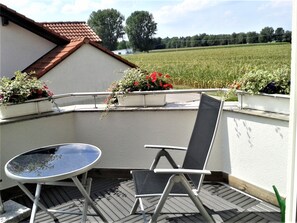 A balcony with a table and chair, potted plants, and a view of a field.