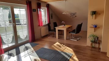 Une pièce avec un plafond en bois, une table à manger avec des chaises, un radiateur et une vue sur l’extérieur, visible à travers une porte vitrée.