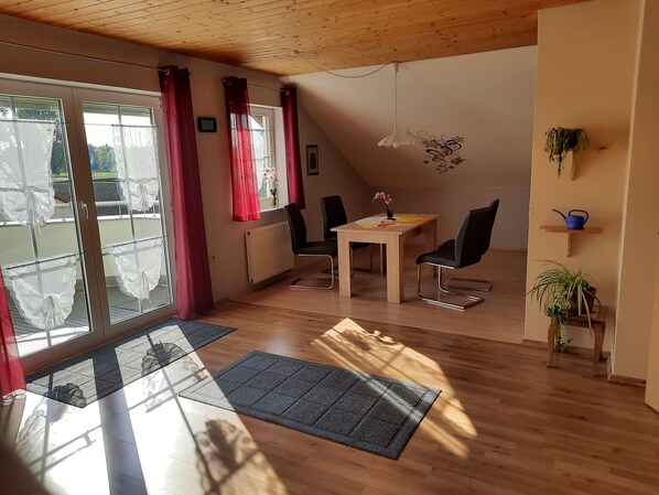 Una habitación con techo de madera, una mesa de comedor con sillas, un radiador y vistas a través de un ventanal.