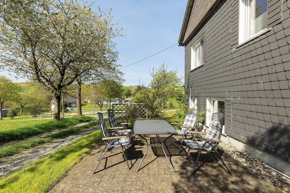 A patio with a table and chairs, a tree, and a house with a grey exterior. - Apartment 'Gänseblümchen' with Private Terrace, Shared Garden and Wi-Fi (Schmallenberg)
