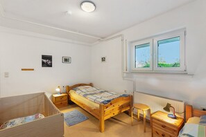 A bedroom with a wooden bed, a desk with a chair, a radiator, and a window with a view of greenery. - Apartment 'Gänseblümchen' with Private Terrace, Shared Garden and Wi-Fi (Schmallenberg)