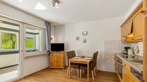A kitchen with wooden cabinets, a dining table with chairs, a television, and a window with a view of greenery. - Apartment 'Löwenzahn' with Shared Terrace, Shared Garden and Wi-Fi (Schmallenberg)