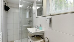 Une salle de bain moderne avec une douche à parois de verre, un lavabo blanc doté d’un distributeur de savon et un miroir au-dessus du lavabo.