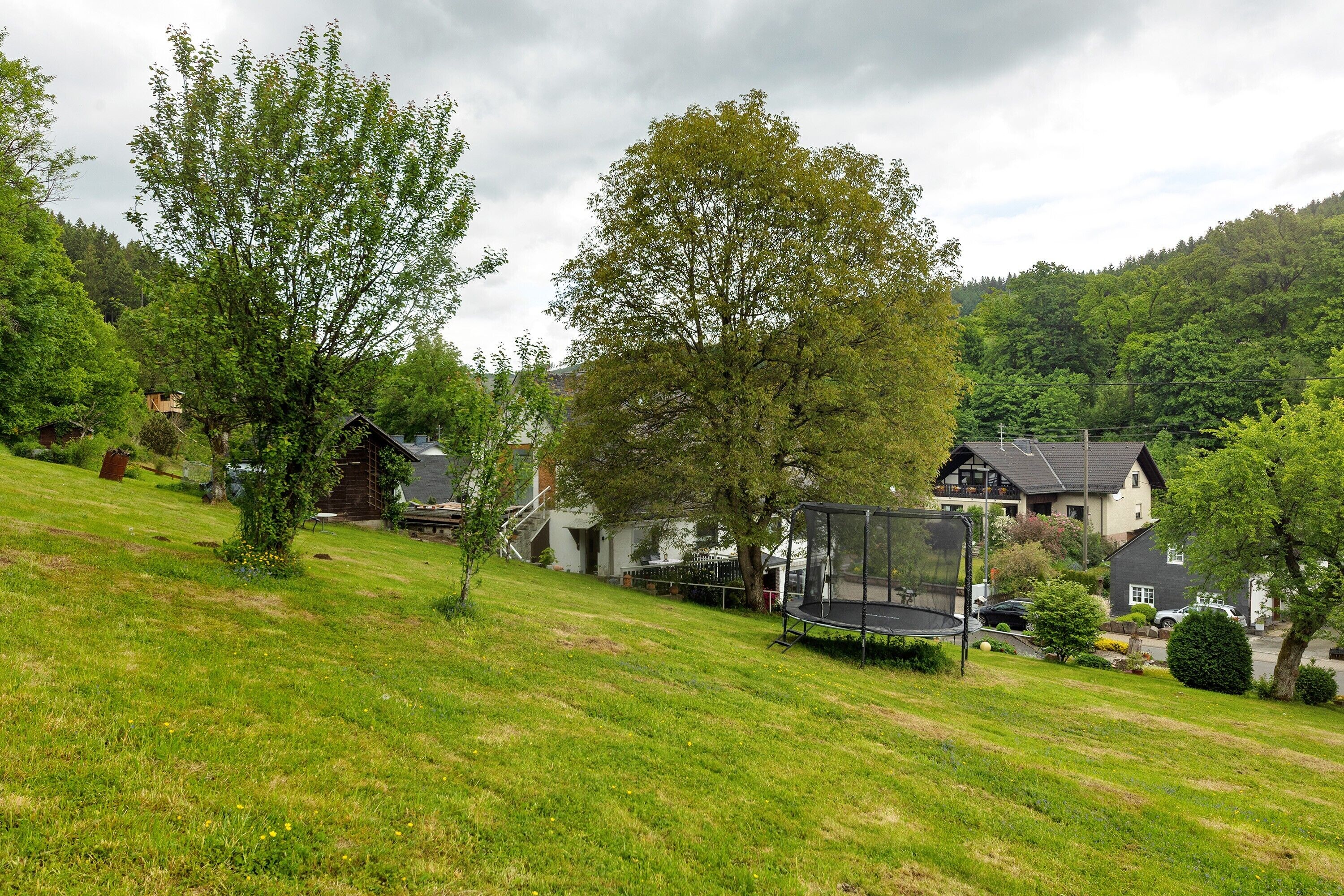 A residential area with houses, a trampoline, and a grassy hill.