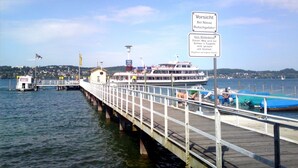 Eine Anlegestelle mit einem vertäuten Boot, ein Schild mit Eiswarnung und Blick auf das Wasser und das entfernte Land.