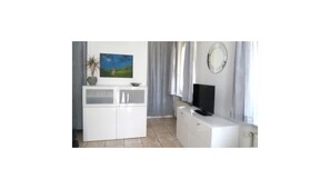 A room with a white cabinet, a flat-screen TV, a painting of a landscape, and a clock on the wall. - Apartment 'Atelier Probst - D5' with Private Terrace, Shared Garden and Wi-Fi (Konstanz)