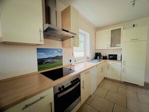 A modern kitchen with a stove, oven, and microwave. There is a window with a view of greenery outside. - Apartment 'Am Kamp' with Mountain View, Private Terrace and Wi-Fi (Schmallenberg)