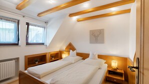 A bedroom with two beds, wooden headboards, bedside tables with lamps, a radiator, and a window with curtains.