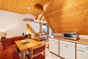 Una cocina acogedora con vigas de madera, un comedor con mesa y sillas, y una kitchenette con microondas.