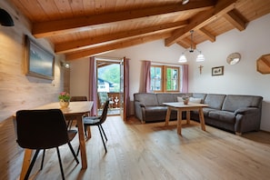 Un plafond en bois, une table à manger avec des chaises, un canapé et une petite table sur laquelle est posé un vase.