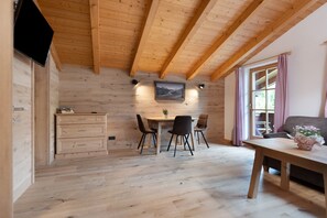 Een houten interieur met een eettafel, stoelen, een aan de muur bevestigde televisie en een raam met gordijnen.