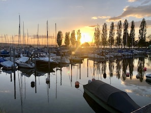 Una marina con imbarcazioni ormeggiate, acqua calma e un tramonto sullo sfondo.