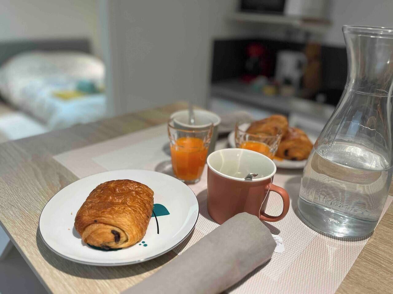 A breakfast setup with a croissant, orange juice, a mug, and a water bottle on a table.