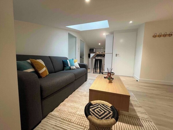 A modern living room with a sofa, coffee table, and a dining area with stools. - To complete (Niort)